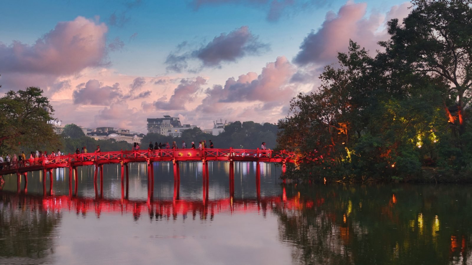 The red Huc Bridge reflecting in the calm green water of Hoan Kiem Lake at twilight in Hanoi
