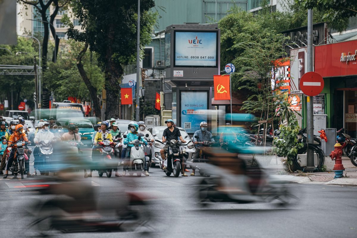 A bustling Hanoi street intersection crowded with motorbikes and scooters during the day