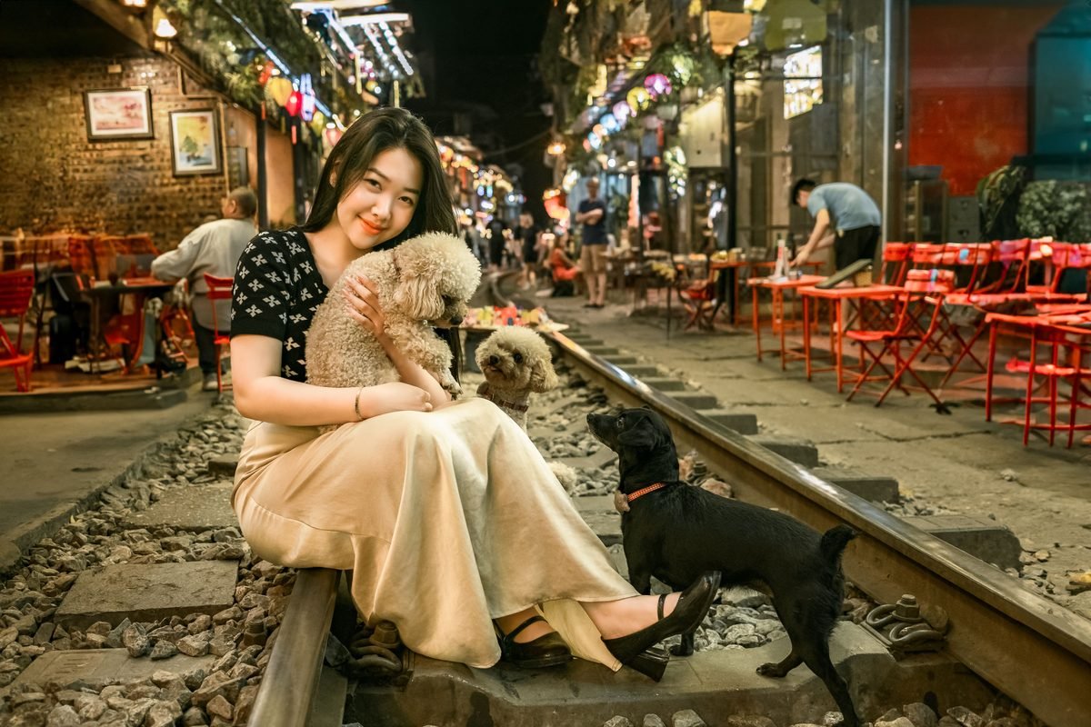 A woman sitting safely on the tracks of the Hanoi train street with pets