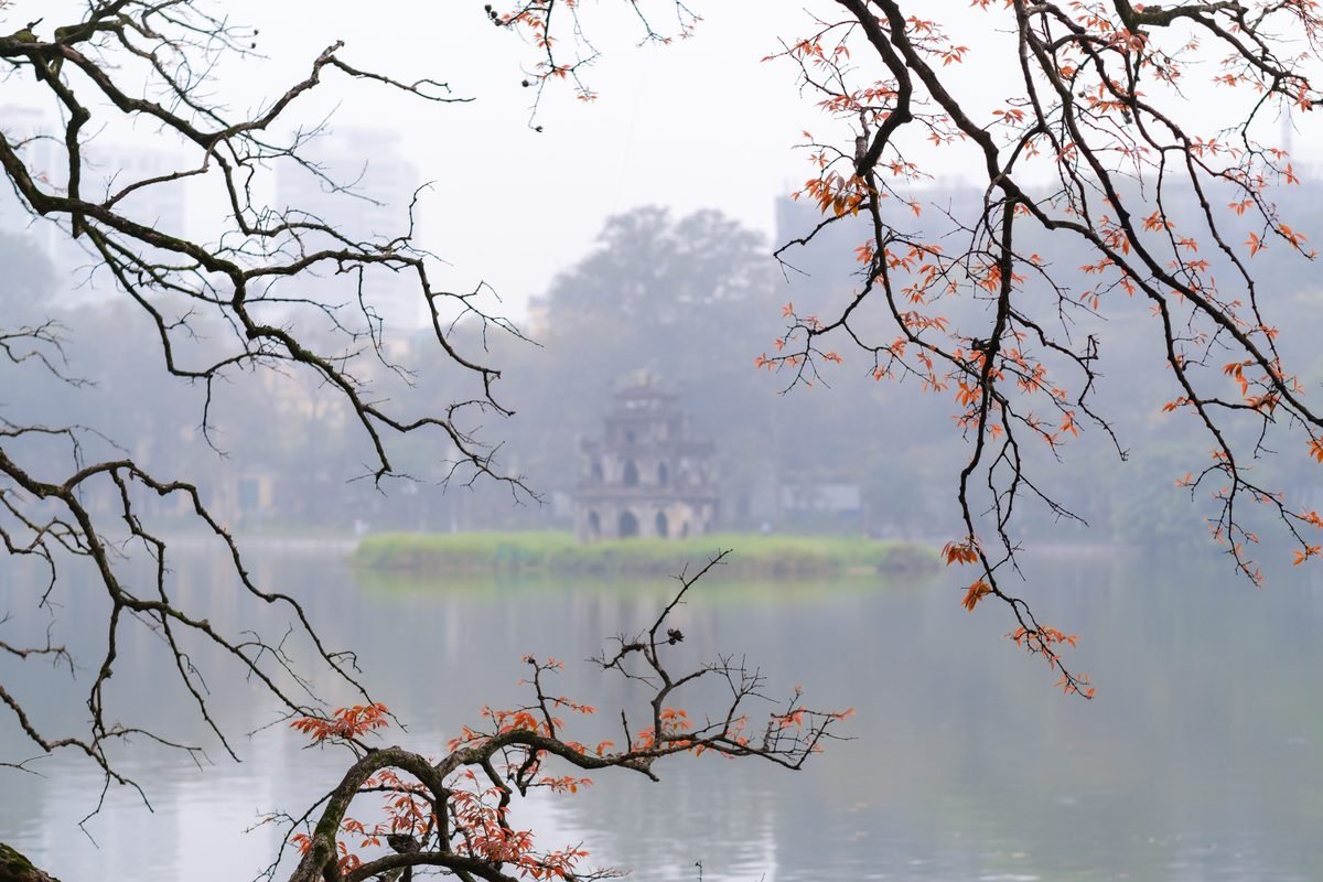 Turtle Tower viewed across Hoan Kiem Lake through misty branches in Hanoi.