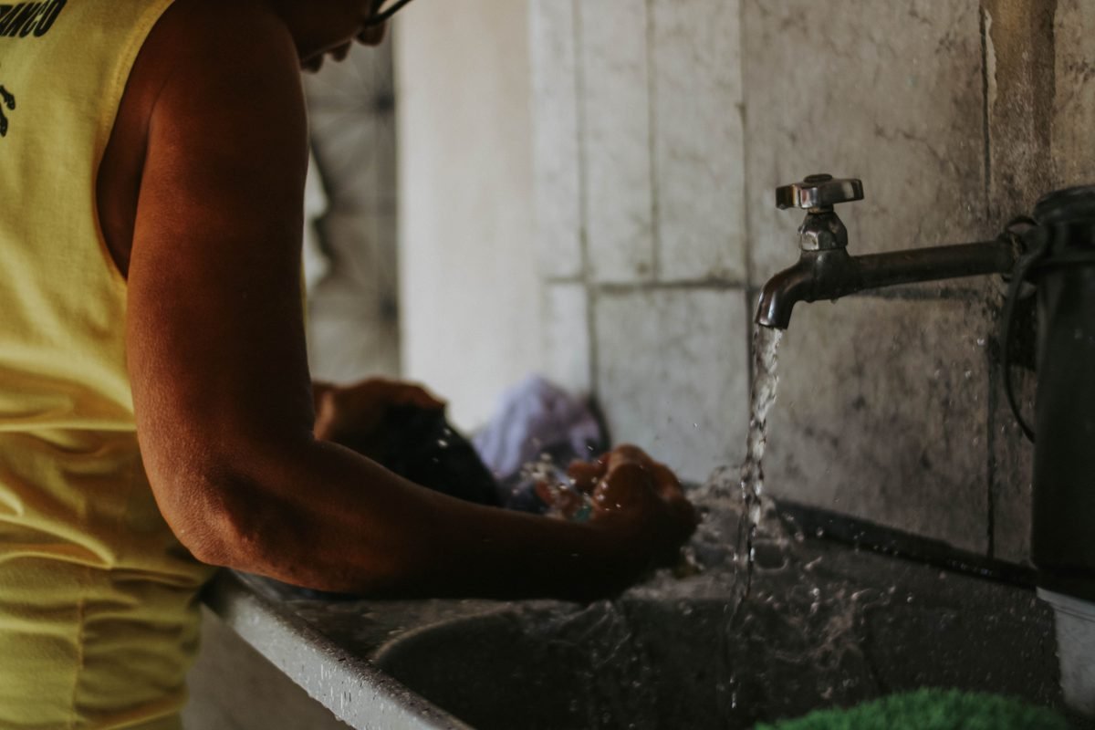 Person washing clothes in a sink with running water.