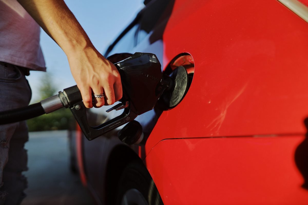 Close-up of a person refueling a red car at an outdoor gas station.