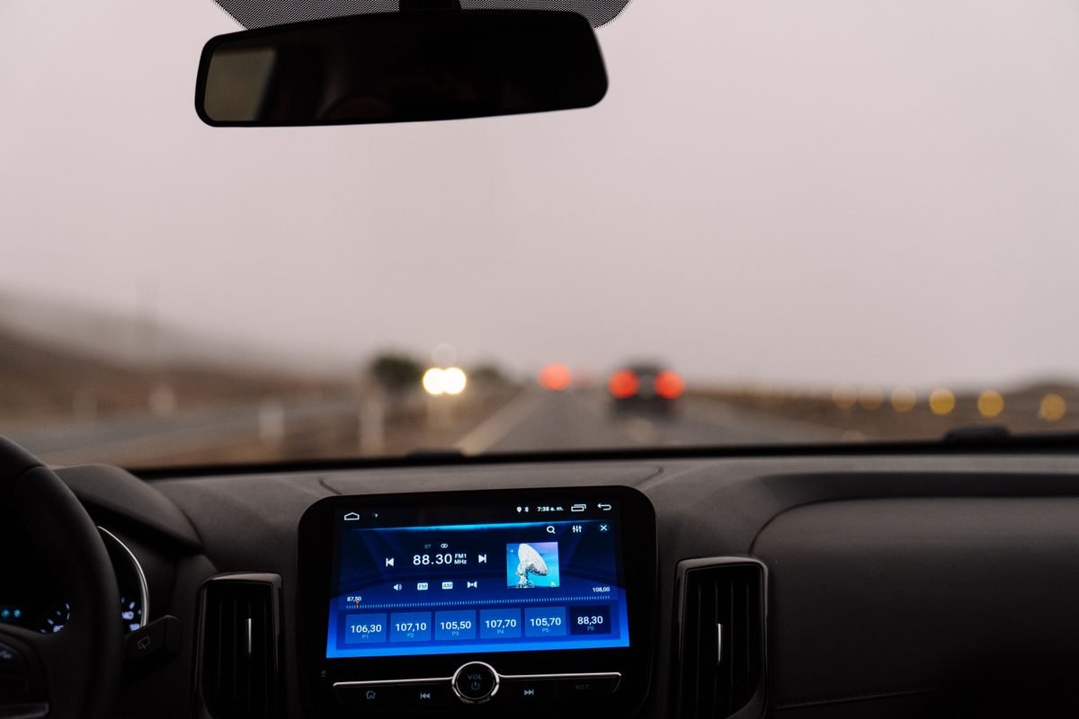 Interior view of a car dashboard and steering wheel on an open road.
