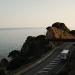 A truck driving along a scenic coastal road overlooking the ocean at sunset.