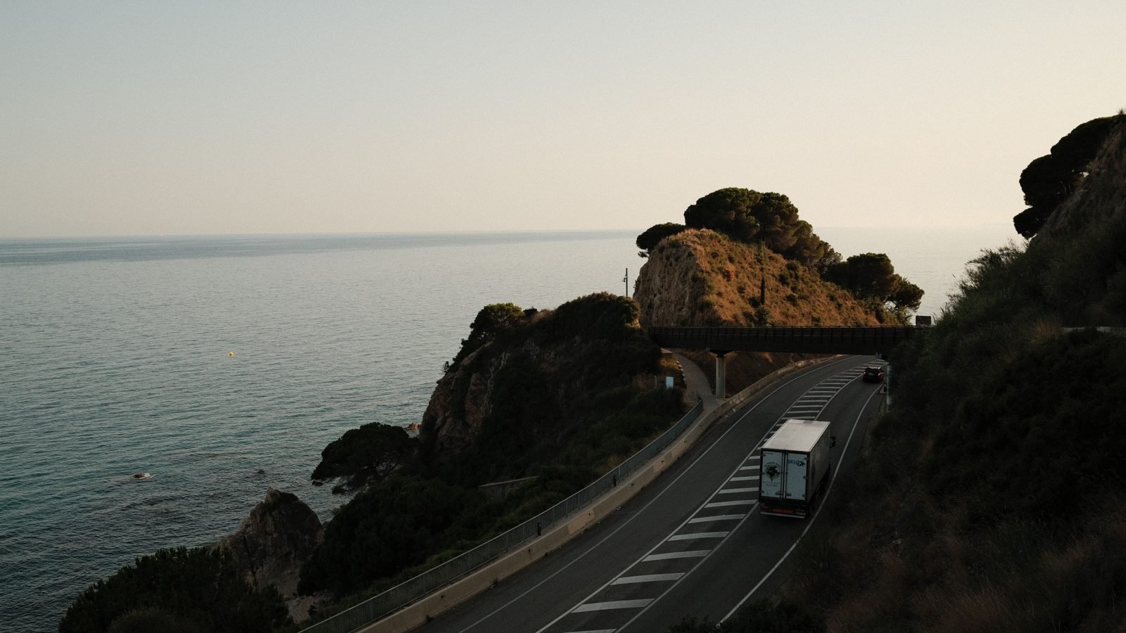 A truck driving along a scenic coastal road overlooking the ocean at sunset.