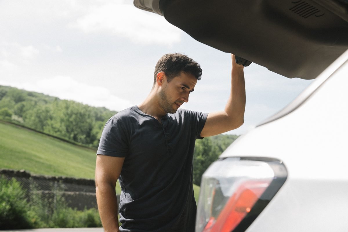 A man examining the open trunk of a car outdoors.