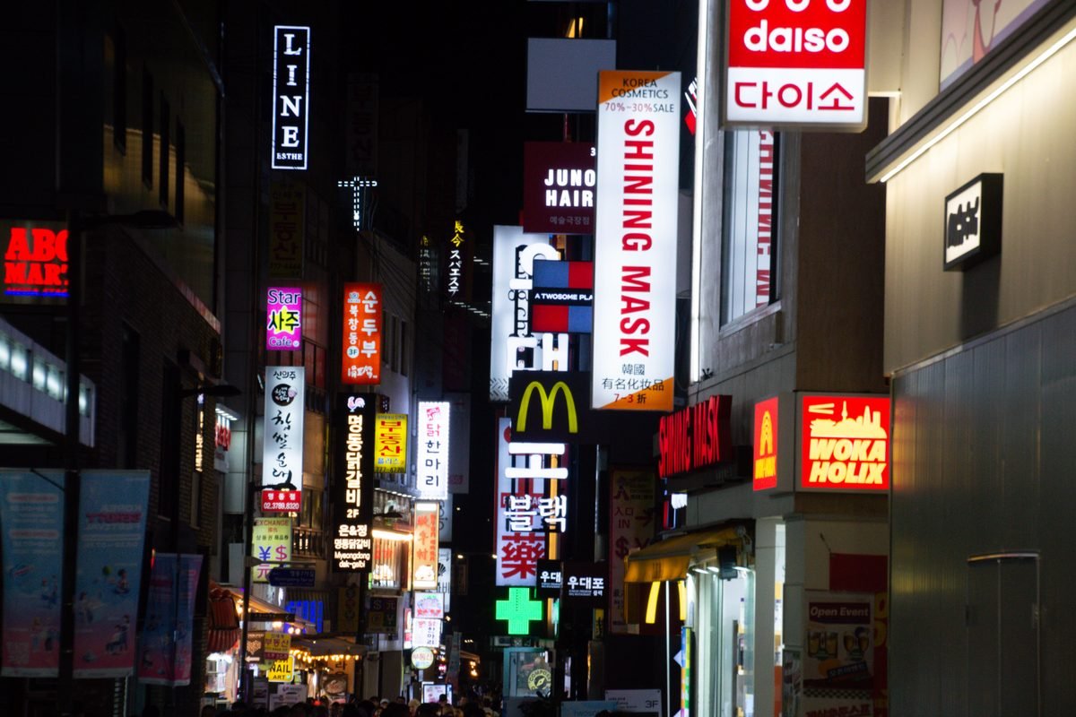 Colorful neon signs light up Seoul's bustling night scene with storefronts.