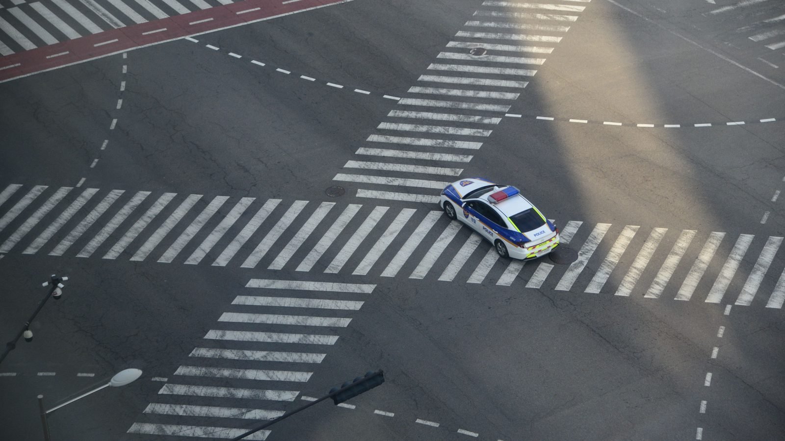 Aerial view of a police car driving through an empty city intersection at dusk.