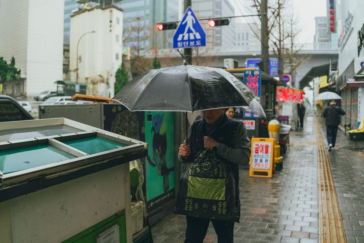 A person walking with an umbrella on a rainy Seoul street.
