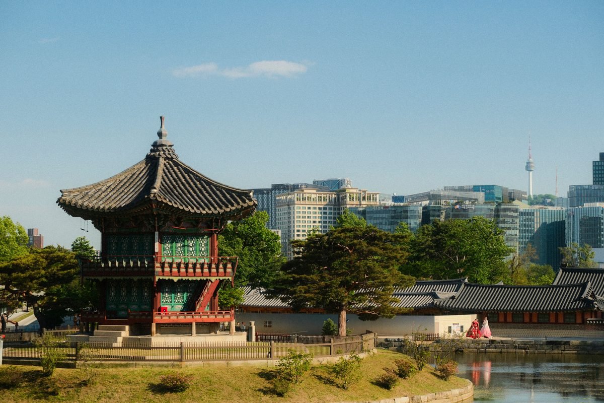 Traditional Korean pagoda near a body of water with N Seoul Tower visible in the distant skyline.
