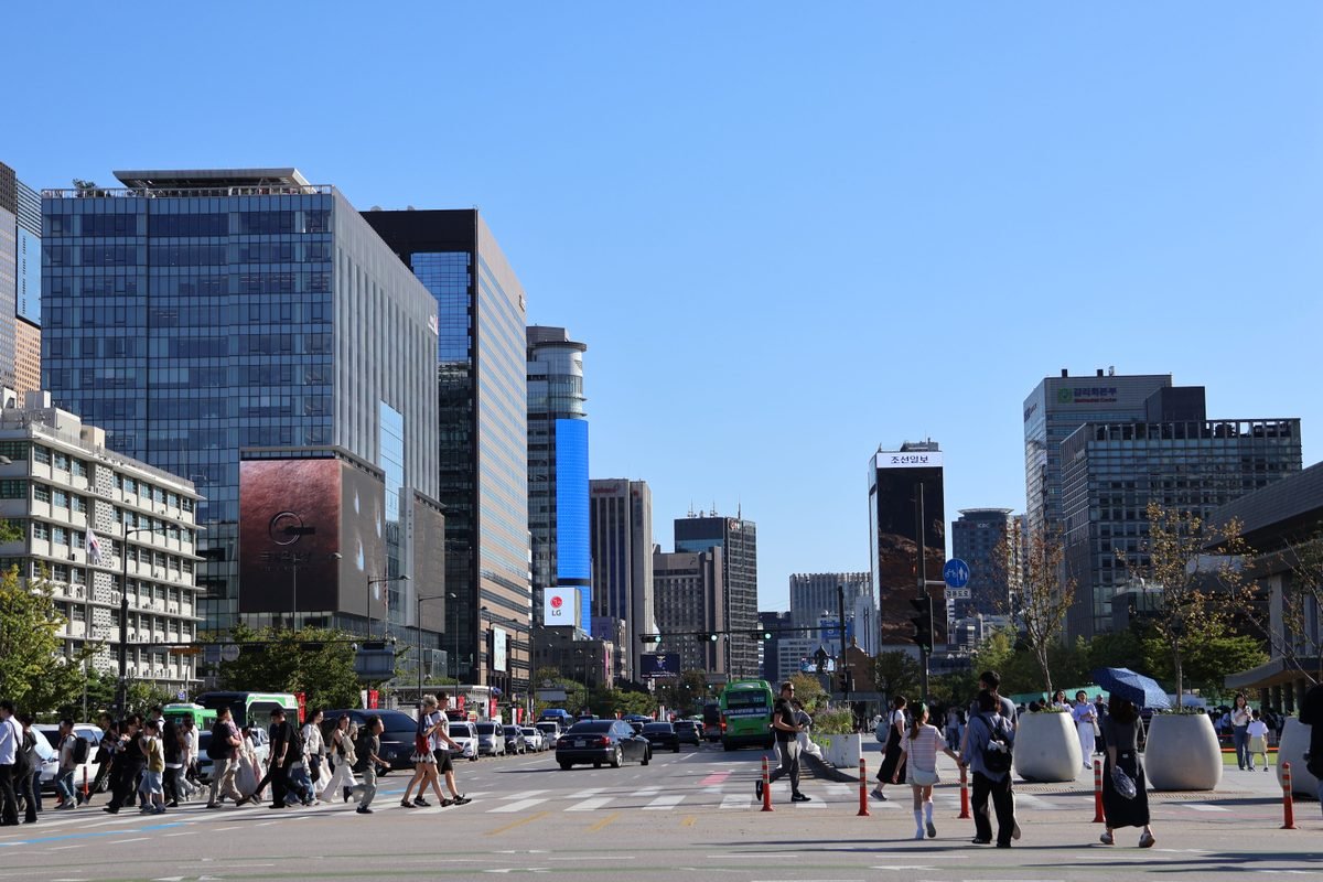Pedestrians crossing a busy street in Seoul with modern skyscrapers