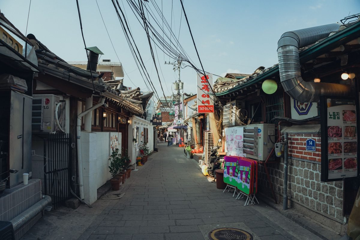 Narrow traditional street in Seoul with overhead cables and shops.
