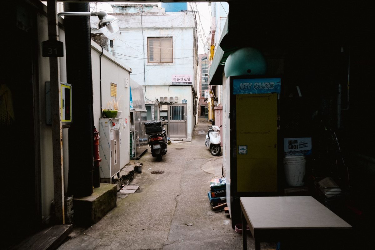 Quiet residential alleyway in Seoul with parked scooter.