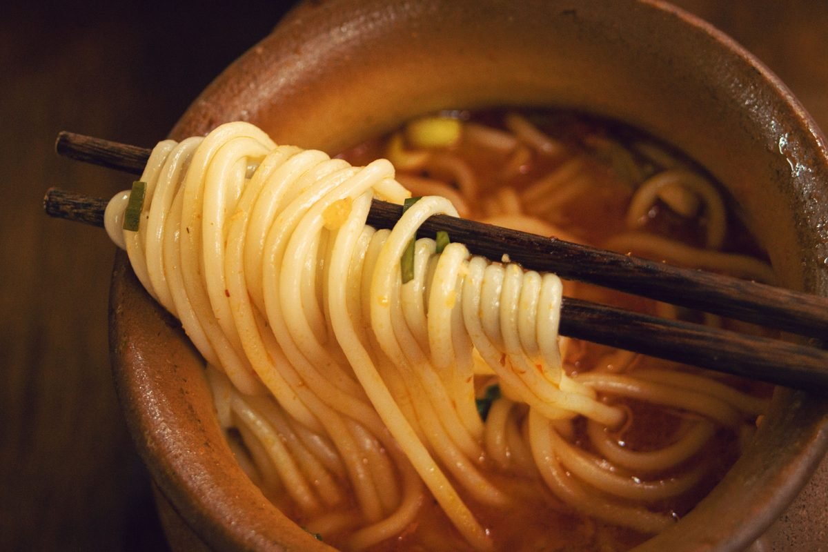 Bowl of Asian noodles being picked up with chopsticks.