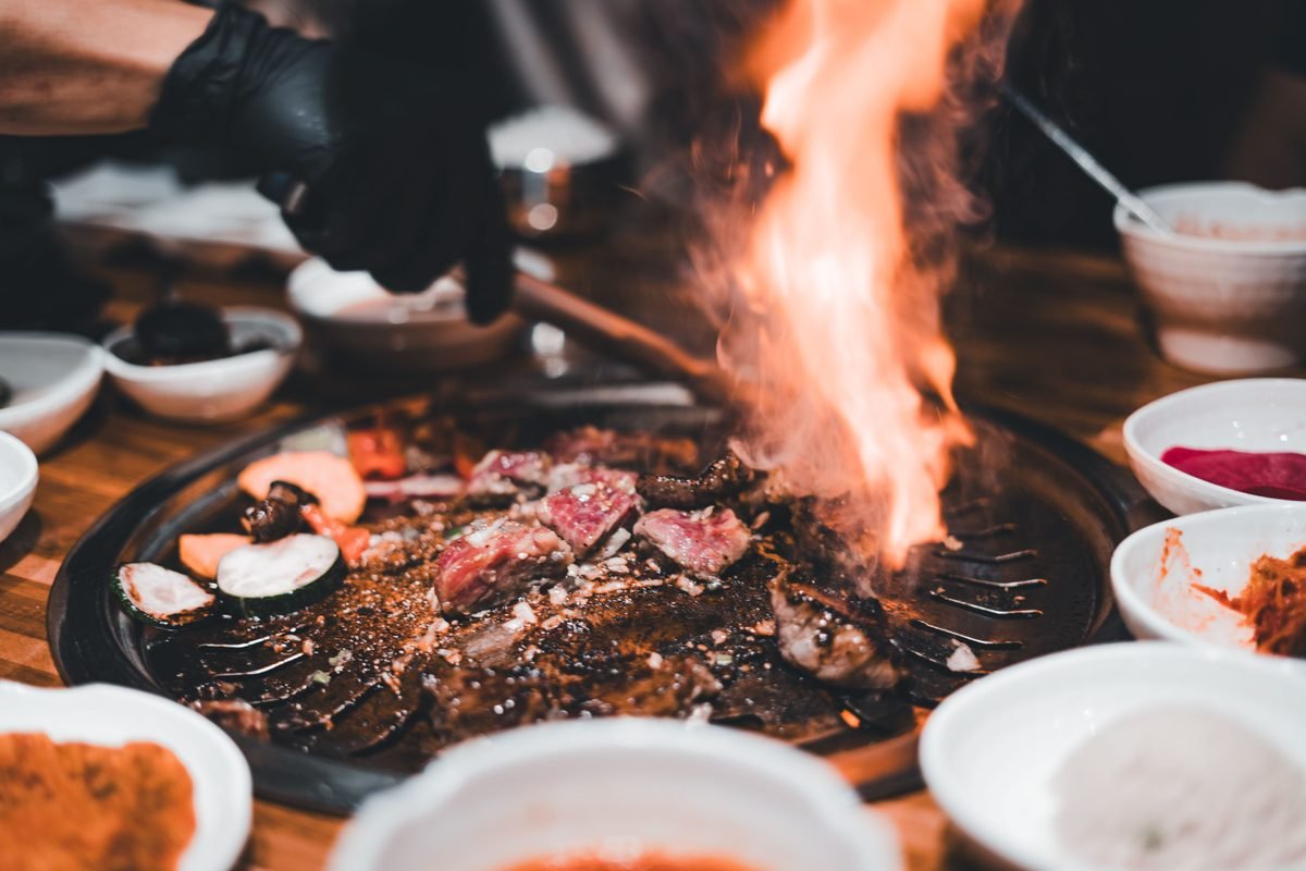Korean BBQ scene showing sizzling meats and flames on a grill