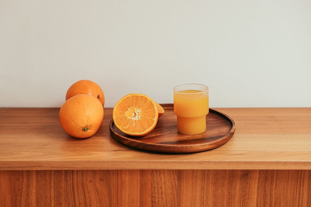 Glass of fresh orange juice with whole and sliced fruits on wooden tray