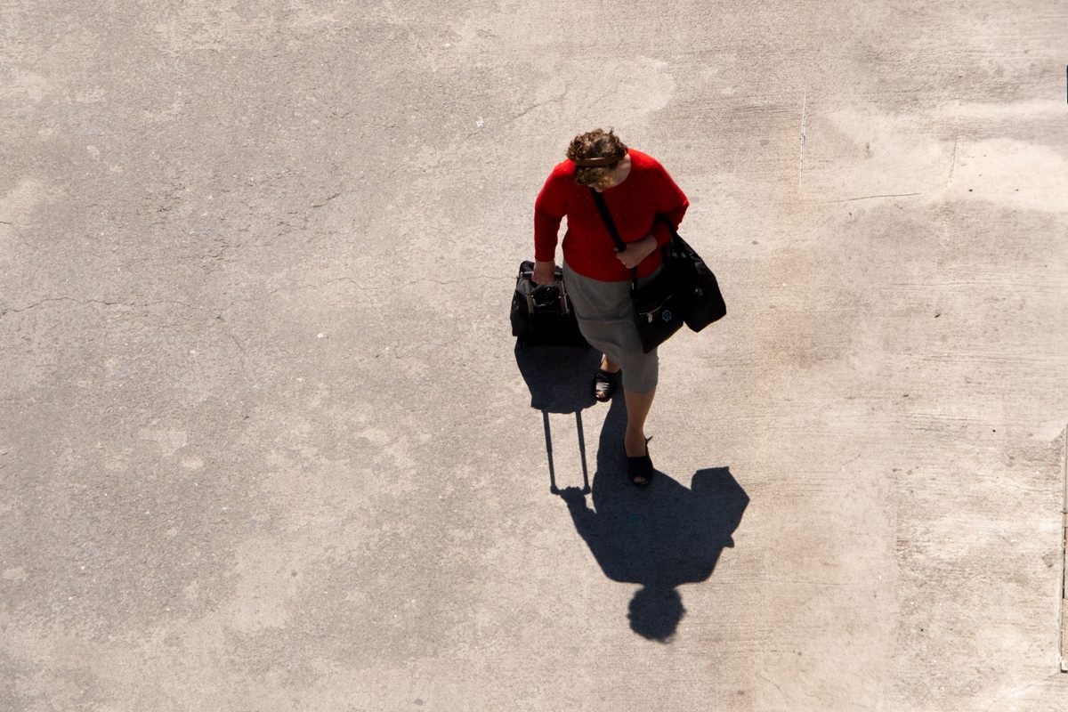Top-down shot of a traveler walking with luggage on a paved surface