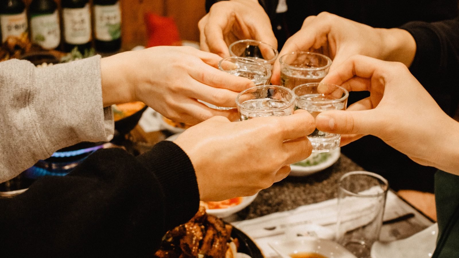Friends clinking soju shot glasses during a celebration.