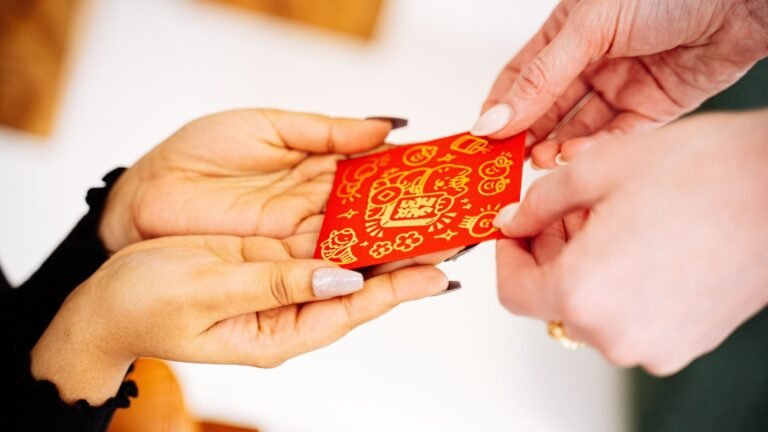 Two hands exchanging a red Lunar New Year envelope indoors.
