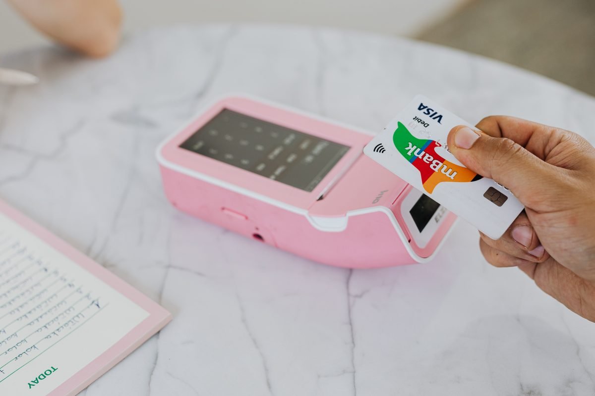 Hand making a contactless payment on a pink card terminal.