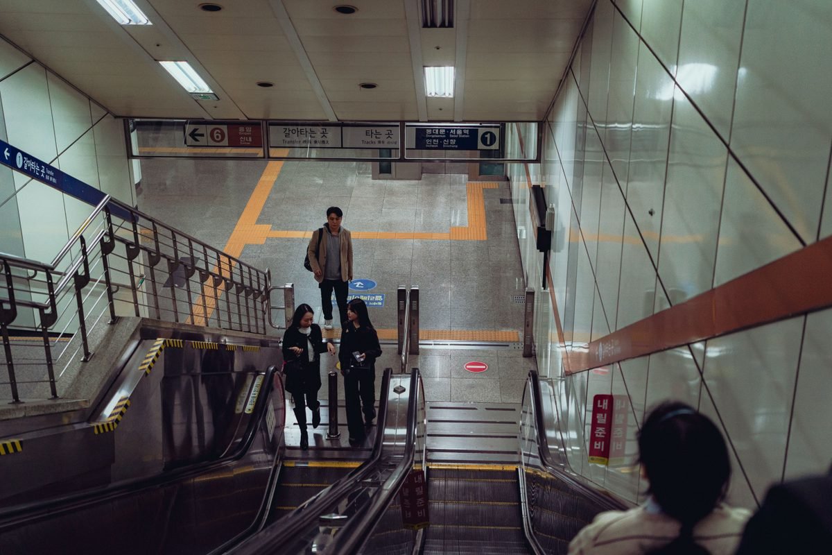 People navigating Suwon subway station stairs in South Korea.