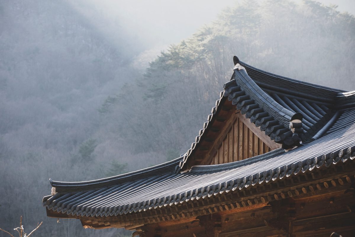 Traditional Korean temple roof against mountain landscape.