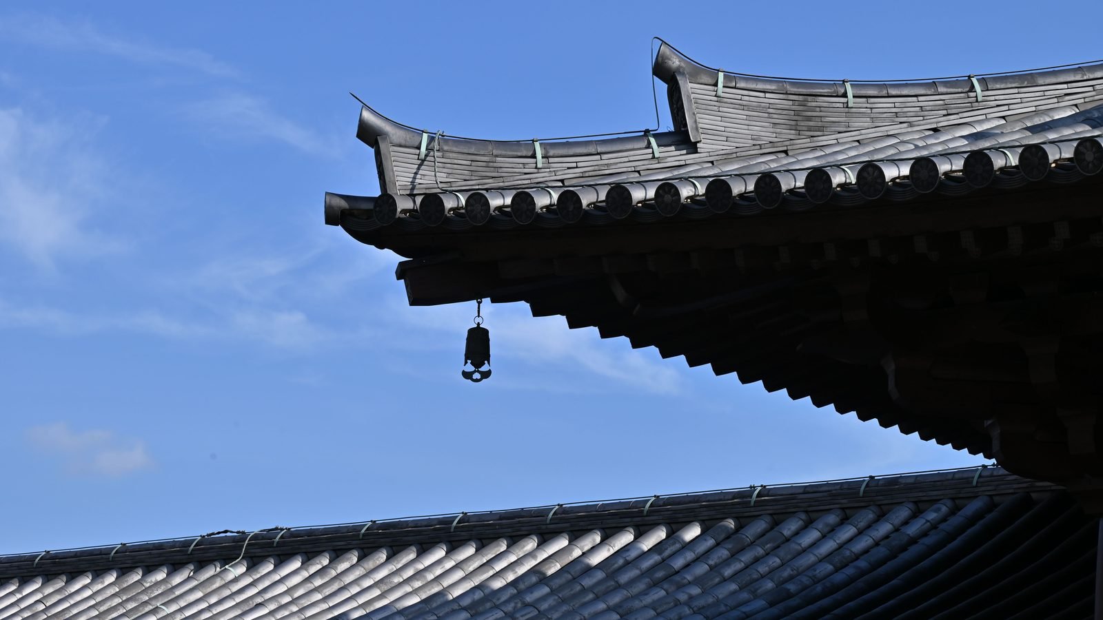 Temple rooftop corner with a hanging bell against a blue sky.