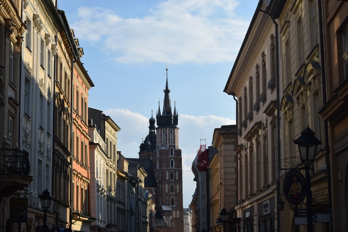 Charming Krakow street view looking toward St. Mary's Basilica tower under a bright sky.