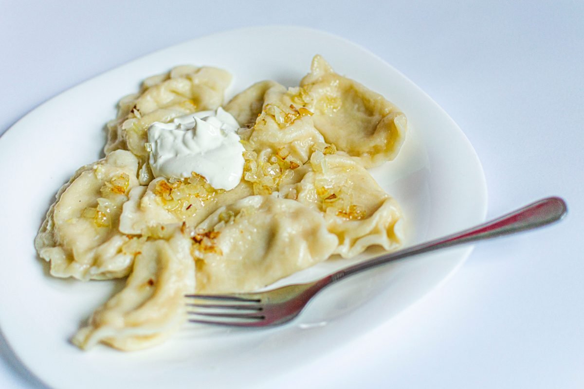 Plate of handmade Polish dumplings with caramelized onions and sour cream on white.