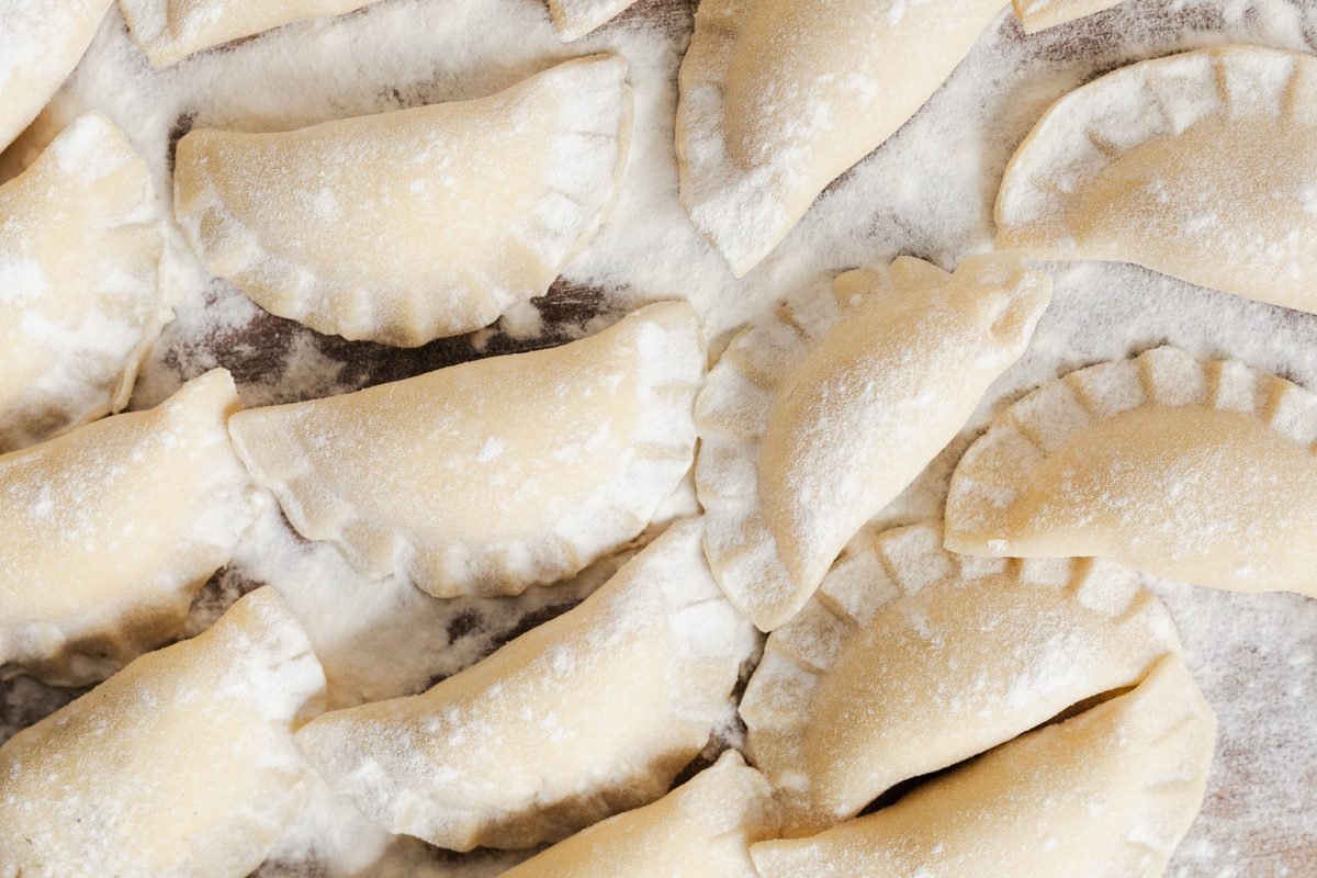 Top view of uncooked pierogi dumplings arranged on a floured surface ready to cook.