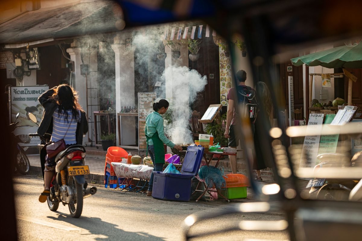 Morning street market scene with food stalls and steam in Luang Prabang.