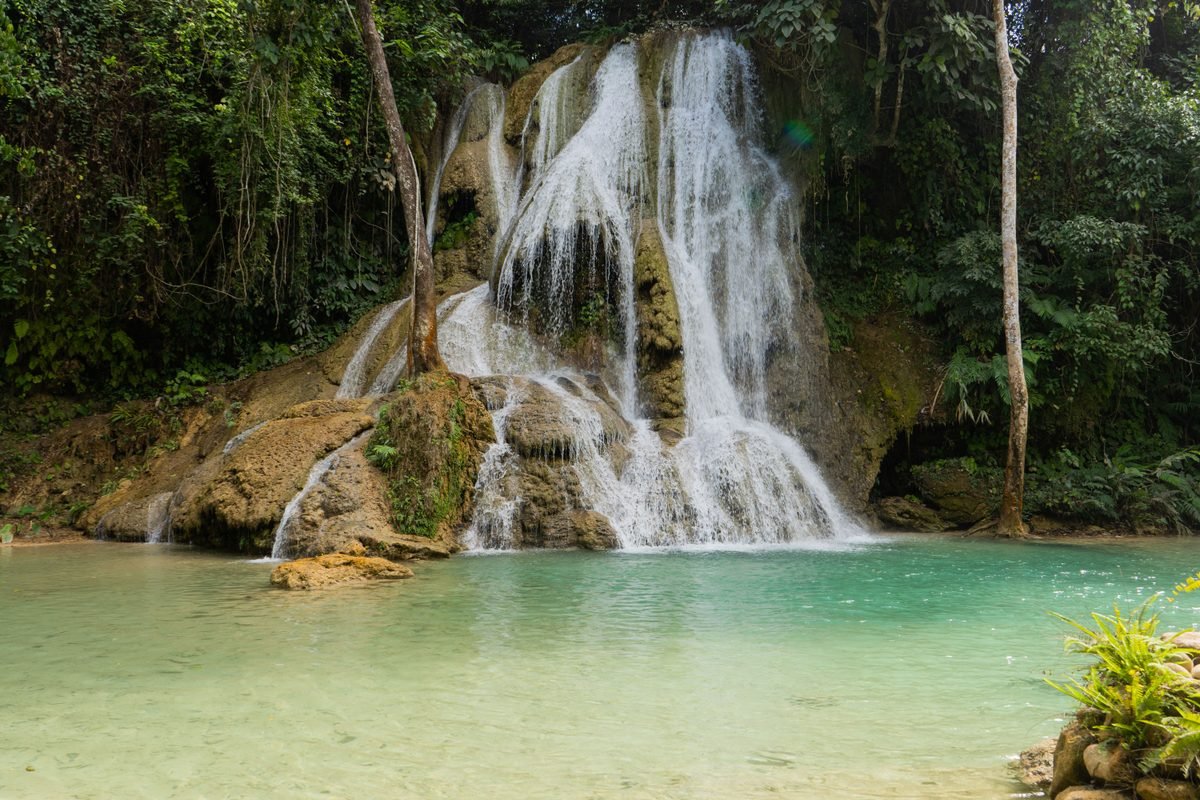 Waterfall cascading into a turquoise pool surrounded by greenery in Luang Prabang.
