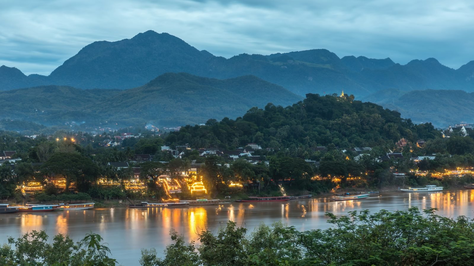 Stunning sunset over the Mekong River and Mount Phou Si in Luang Prabang, Laos with traditional boats.