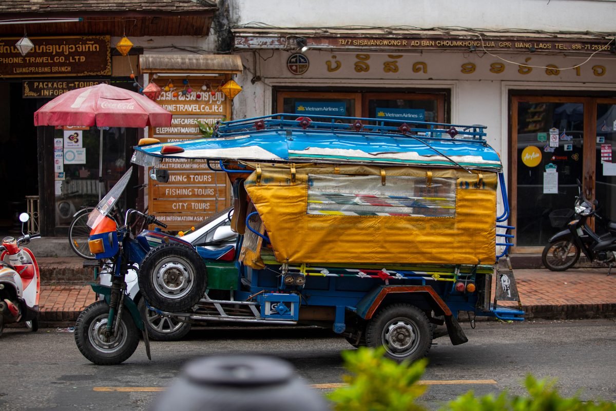 Colorful blue and yellow auto rickshaw tuk-tuk parked on a street in Luang Prabang.