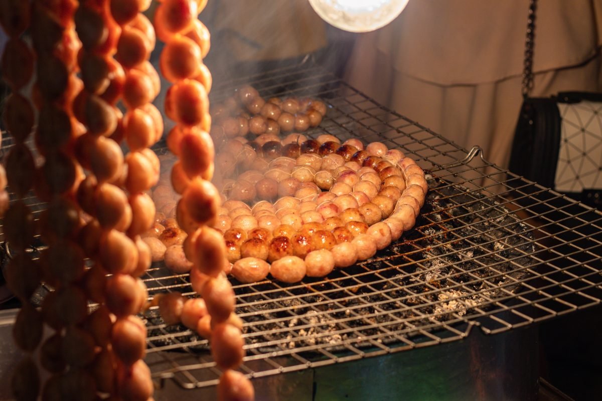 Traditional grilled sausages cooking on a barbecue grill at a night market.