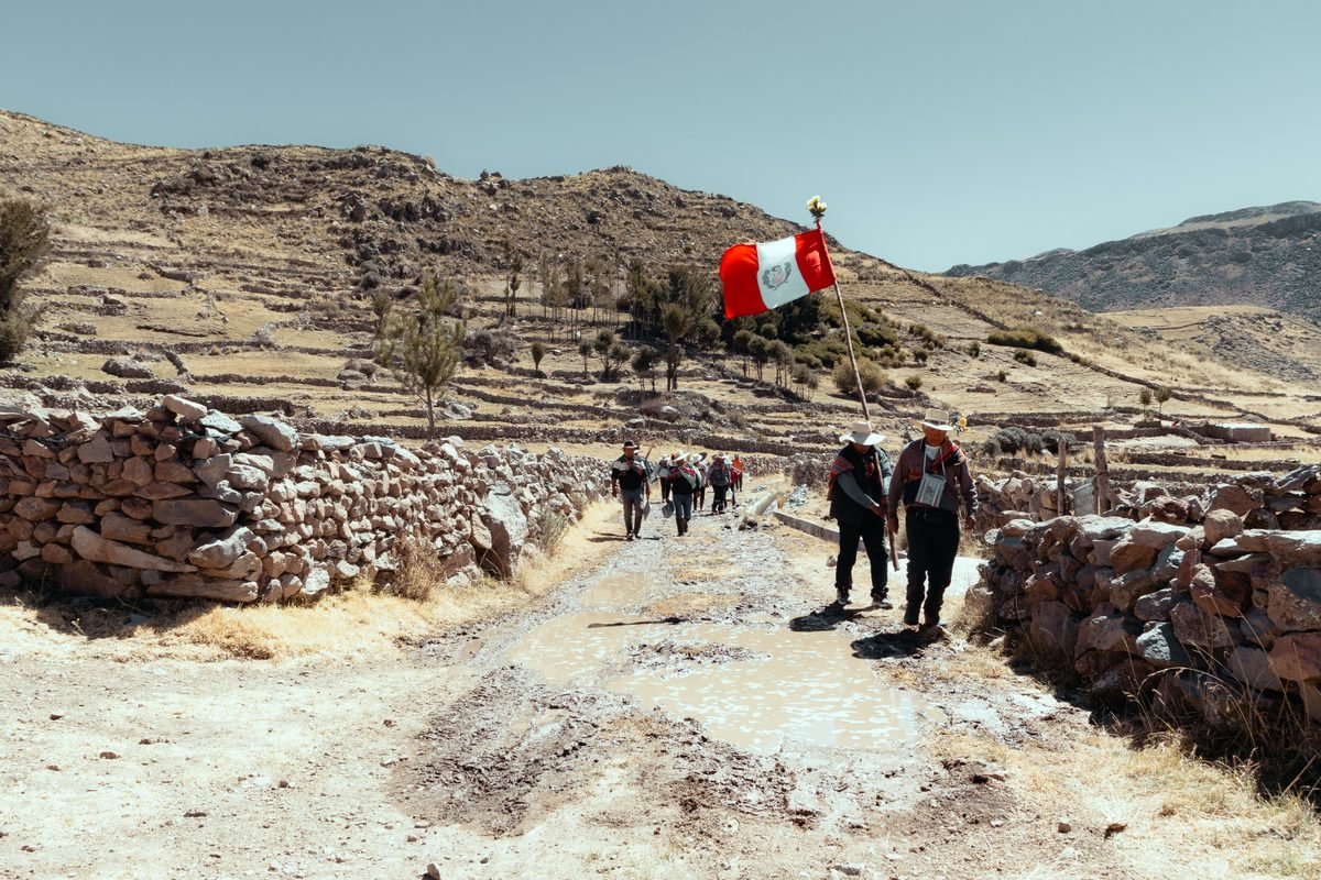 Travelers walking along an Andean stone path carrying a Peruvian flag