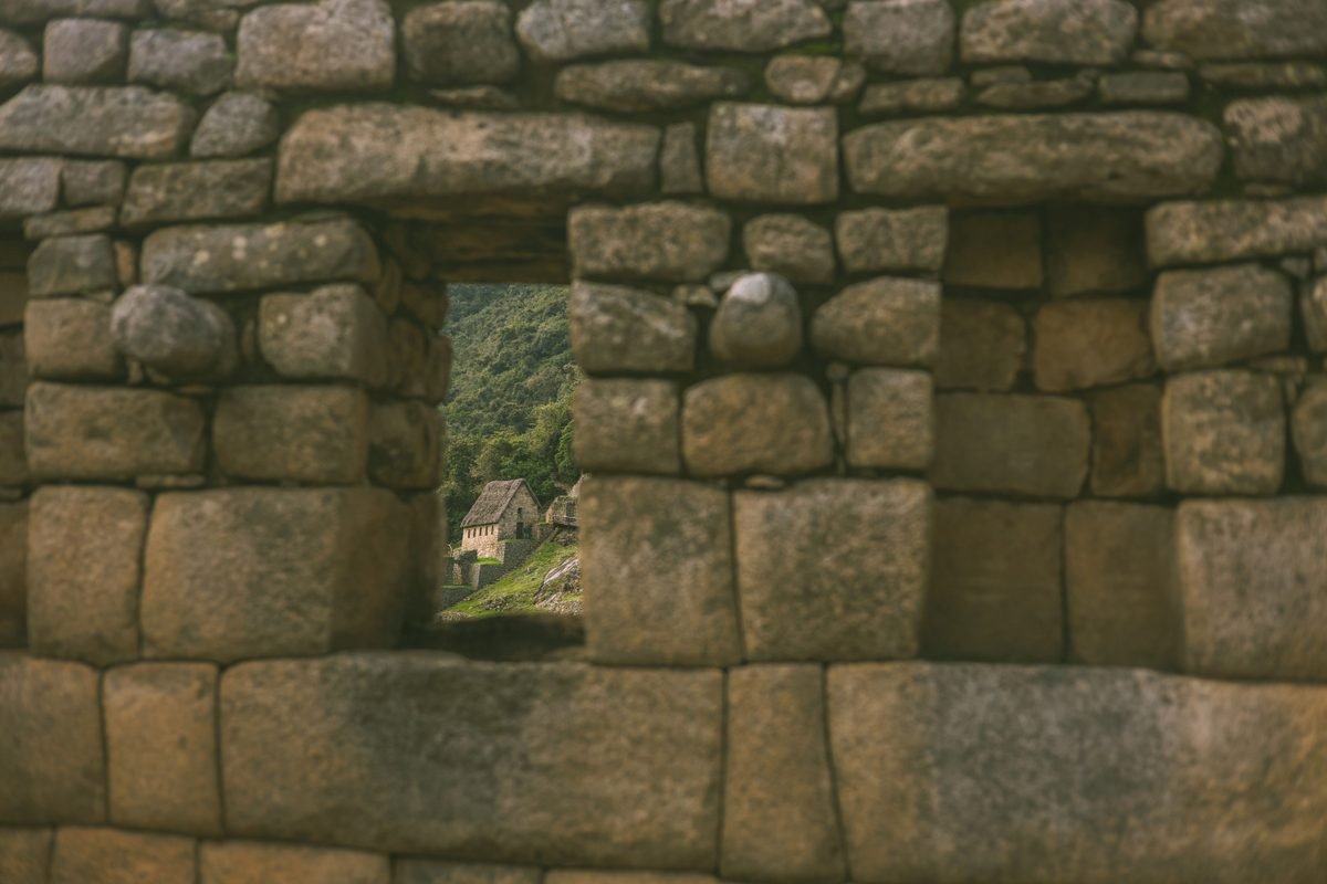 View looking through a weathered stone window frame at Machu Picchu ruins