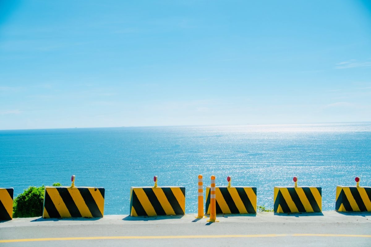 Bright yellow and black striped road barriers overlooking the sparkling sea.
