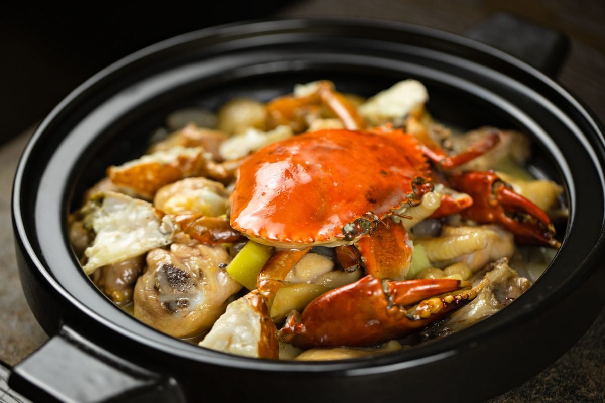 Savory seafood stew with crab and mushrooms served in a black pot.