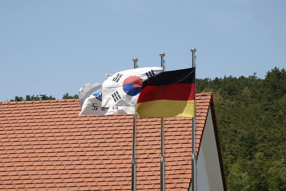 South Korean and German flags flying on a flagpole above a red-tiled roof in Namhae