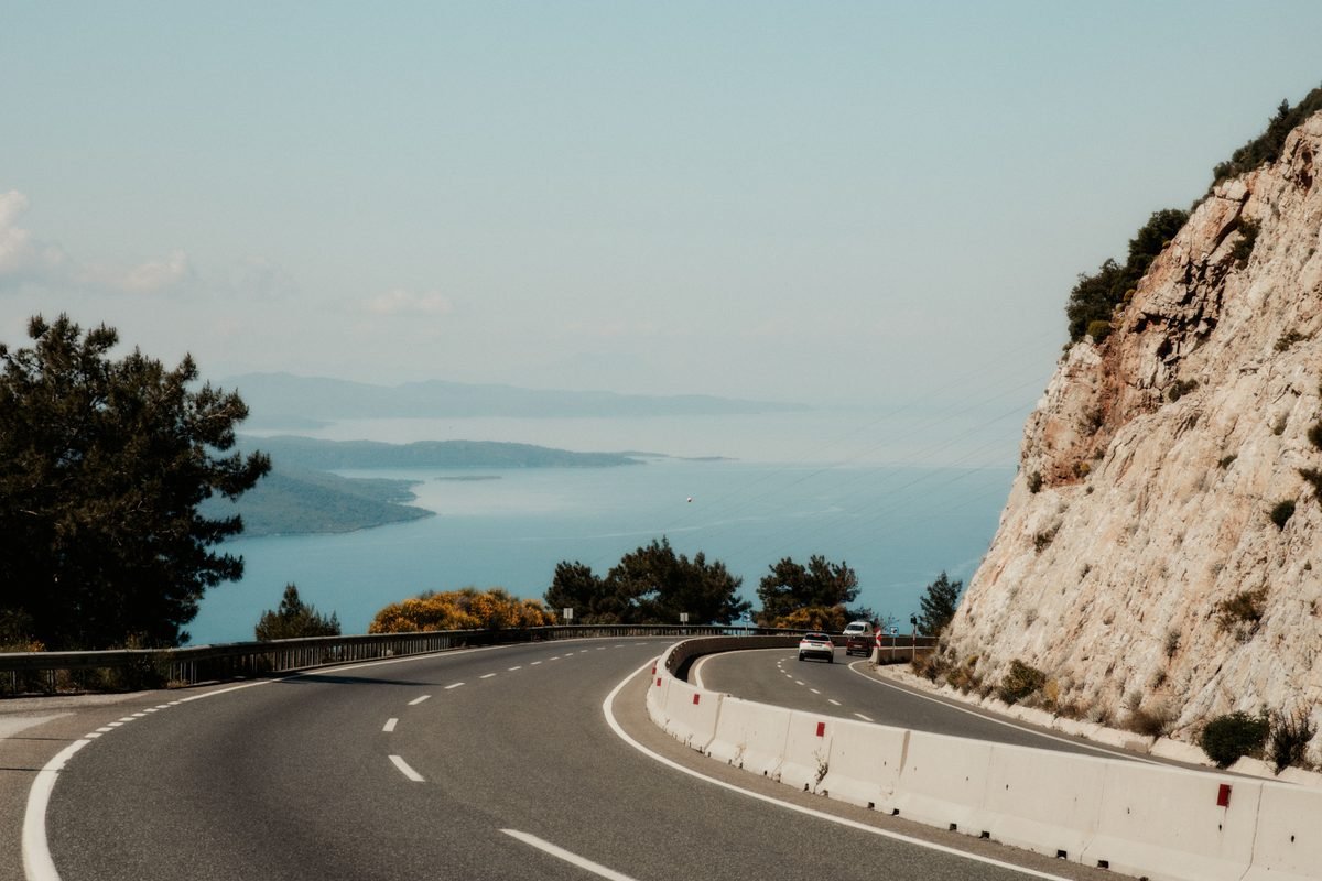 Winding road hugging a rocky cliff with an ocean view on an overcast day