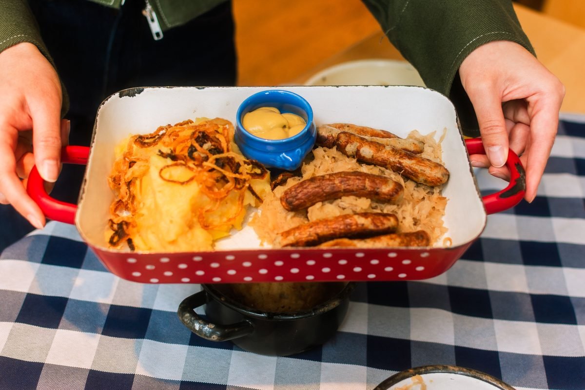 Tray of German sausages with sauerkraut and mustard held over a checkered tablecloth