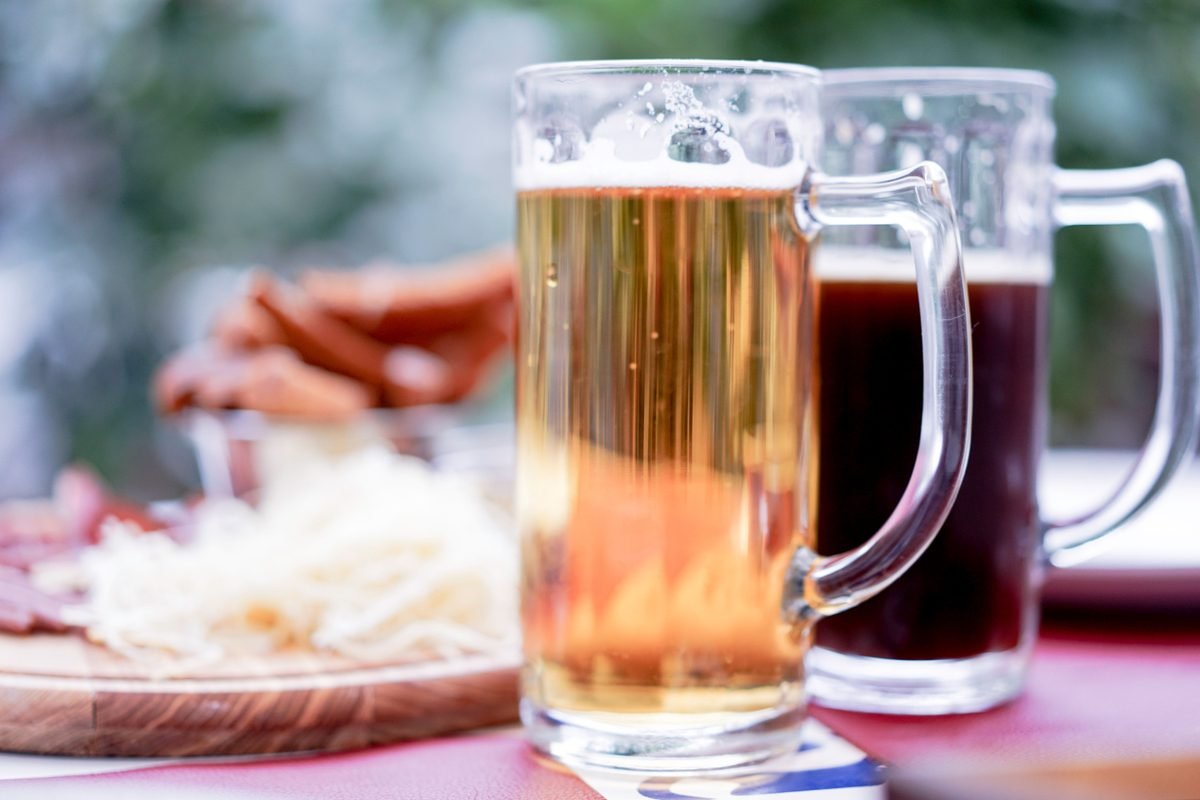 Two large mugs of light and dark beer served on an outdoor table