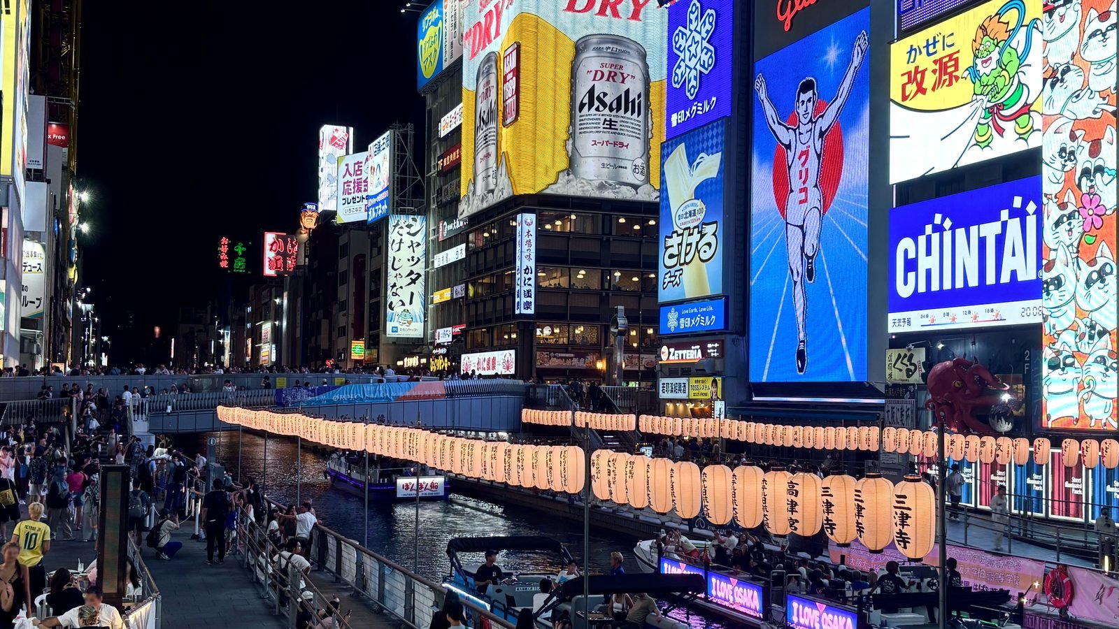 Dotonbori canal at night with the glowing Glico Man neon sign and colorful advertisements in Osaka