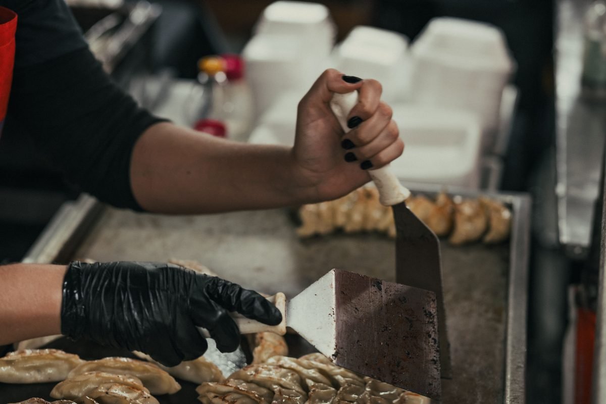 Hands using spatulas to prepare food on a hot griddle