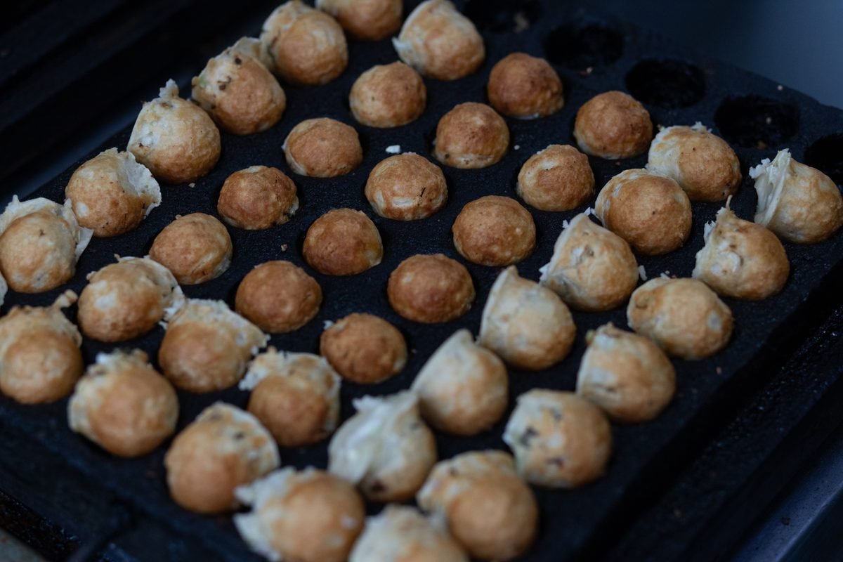 Takoyaki balls cooking in a rounded iron griddle pan