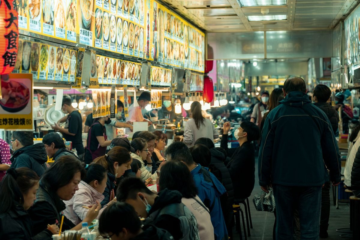 Crowded indoor hawker center with people eating at tables