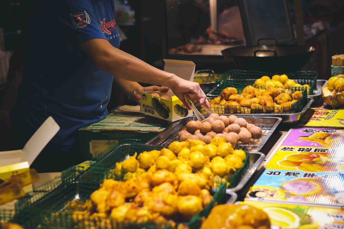 Street food vendor handling fried snacks at a night market stall