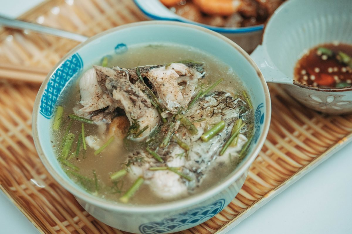 Steaming bowl of fish soup garnished with herbs in a ceramic bowl