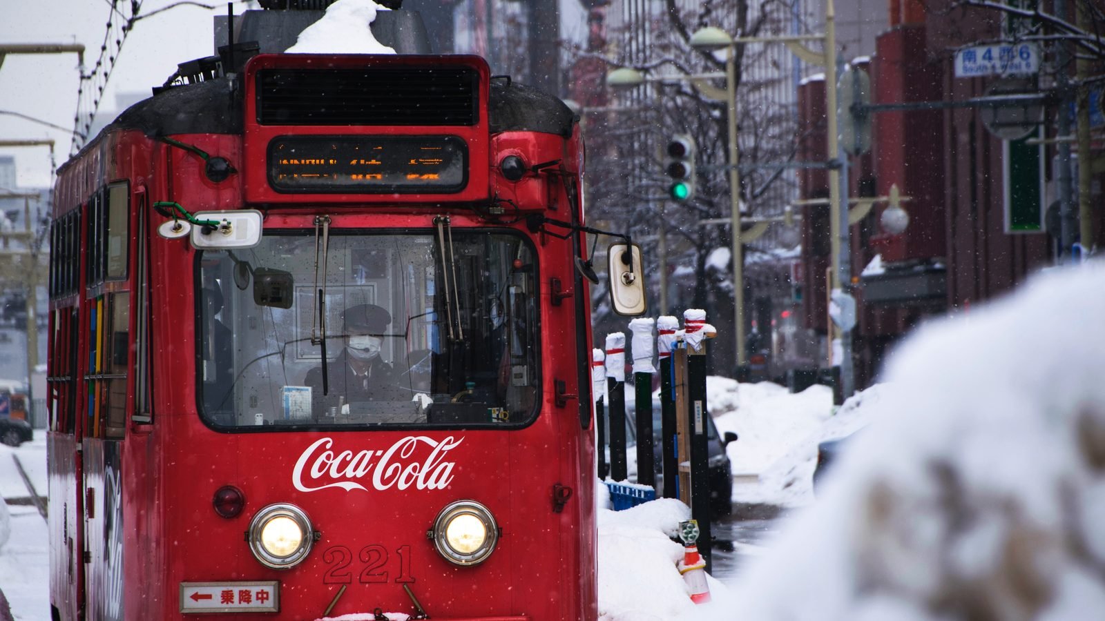 A red tram driving through a snowy street in Sapporo during a snowstorm.